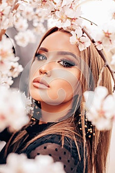 Girl with blond hair in elegant clothes and earrings posing among flowering peach trees