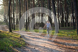 A girl with blond hair runs along a forest path jumping over all the branches in the morning