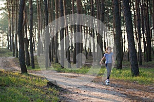 A girl with blond hair runs along a forest path jumping over all the branches in the morning