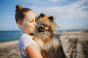 Girl with blond hair with smile hugs pomeranian dog with golden hair on seashore near Black Sea