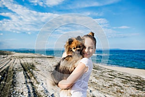 Girl with blond hair with smile hugs pomeranian dog with golden hair on seashore near Black Sea