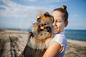 Girl with blond hair with smile hugs pomeranian dog with golden hair on seashore near Black Sea