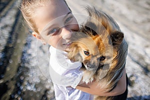 Girl with blond hair with smile hugs pomeranian dog with golden hair on seashore near Black Sea