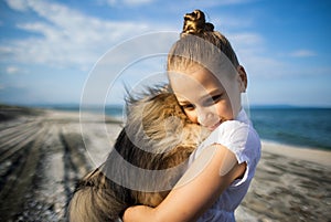 Girl with blond hair with smile hugs pomeranian dog with golden hair on seashore near Black Sea