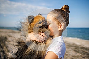 Girl with blond hair with smile hugs pomeranian dog with golden hair on seashore near Black Sea