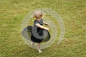 Girl with blond hair spin in black dress on grass