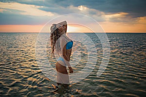 Girl with blond hair in a swimsuit posing against the backdrop of the sunset in the estuary enjoying nature around him