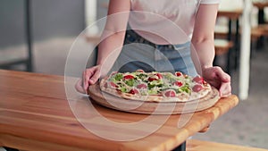 a girl with blond hair and a white shirt carries a pizza to serve on the table