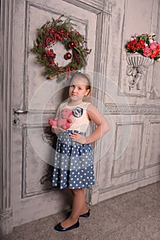 Girl blonde child with a pink teddy bear in hand with a Christmas wreath