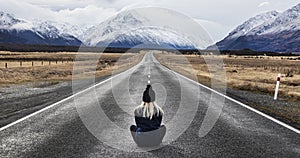 Girl with blonde hair wearing a hat sits in the middle of the road in New Zealand