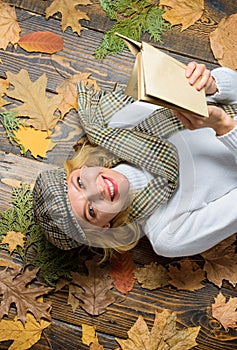 Girl blonde lay wooden background with leaves. She likes detective genre. Woman lady in checkered hat and scarf read