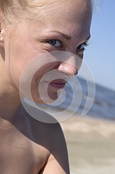 Girl blonde smiling, looking into the camera. Girl on a background of sea water and sandy beach. Beautiful young woman