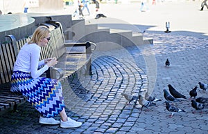 Girl blonde woman relaxing city square and feeding pigeons. Woman tourist or citizen toss crumbs for pigeons. Group