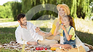 Girl blowing bubbles enjoying day with parents in park