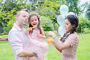 Girl blowing bubbles with her father and mother in park