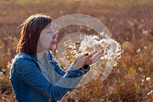 Girl blowing fluff cattail in her hands.