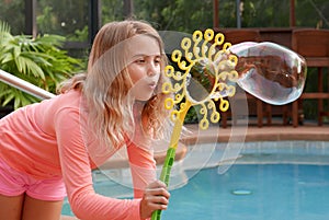 Girl blowing a large soap bubble outside by a swimming pool