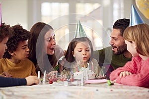 Girl Blowing Out Candles On Birthday Cake At Party With Parents And Friends At Home