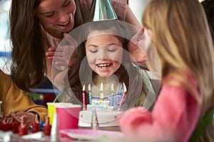 Girl Blowing Out Candles On Birthday Cake At Party With Parents And Friends At Home
