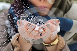 Girl blowing on snow in her hands in winter.Glamorous colorful manicure