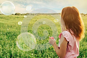 Girl blowing soap bubbles in summer at sunny day