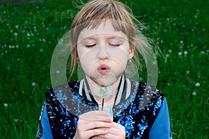 A girl blows on a dandelion. A child in a blue jacket blows on dandelion seeds