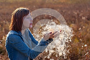 The girl blows the fluff of a cattail in her hands and he falls down.