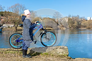 A girl with a blue bicycle on the shore of a pond