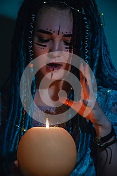 Girl with blue dreadlocks conjures at night in a dark room, candle fire and a cow skull.