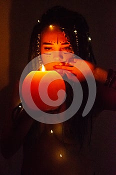 Girl with blue dreadlocks conjures at night in a dark room, candle fire and a cow skull.