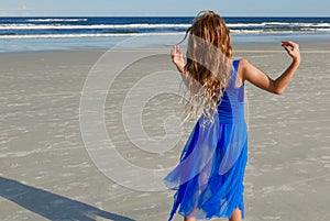 Girl in a blue dress dancing on the beach in front of the ocean