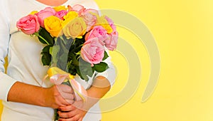 A girl in the blue dress holding beautiful tender blossoming bouquet of yellow and pink roses on yellow background. Flowers