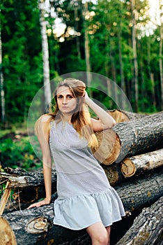 Girl in a blue dress near a fallen tree on a background of a forest in summer weather, a wooden spittle of a tree