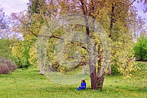 A girl in a blue dress reading a book in a spring Park. A woman in a straw hat sitting on the grass spring forest