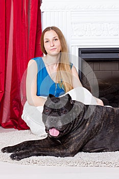 Girl in blue dress sitting by the fireplace with dog Cane Corso