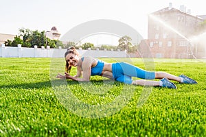 Girl in blue fitness clothes lying on grass stadium. Brunette advertises green lawn on football field. Woman has sporty lifestyle