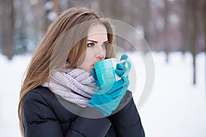A girl in blue gloves drinks tea from a blue cup