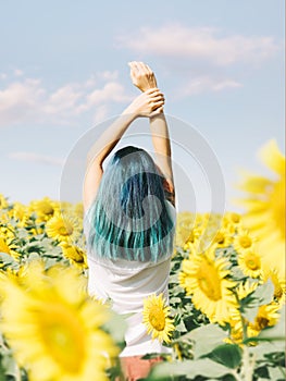 Girl with blue hair relaxing in sunflowers field.