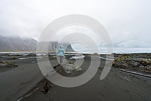 Girl with blue jacket  are standing on a sand dune in Stokksnes looking towards the Vestrahorn mountain chain