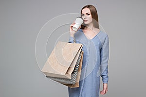 Girl in blue jamper drinking coffee with paper shopping bags