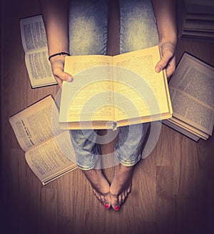 The girl in blue jeans holding a book sitting on the floor,books lying around her ,Student learning study reading close up retro