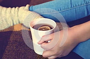 A girl in blue jeans holds a cup of tea and lemon in her hand. Close-up, soft focus