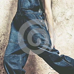 Girl in  blue jeans jumpsuit against grunge wall indoor lower body