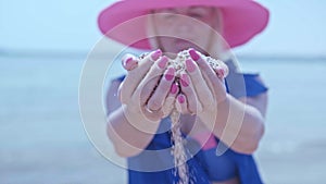 A girl in a blue pareo and a pink hat throws sand through her fingers not on the seashore.