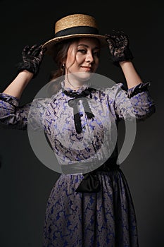 A girl in a blue retro dress in the style of the 1900s. A woman adjusts her hat in lace gloves. Historical fashion of