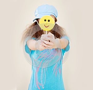 Girl in blue shirt and cap with two tails holds in front of a big yellow candy