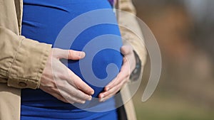 Girl in blue shirt with maternal tenderness carees affectionately carees her big stomach with child, Steady cam, slow mo