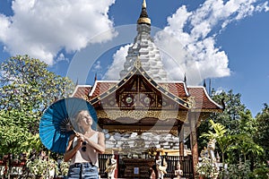 Girl with a blue umbrella in her hands with a comfortable expression sunbathing in front of a Buddhist temple