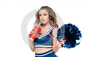 Girl in blue uniform holding pompom and drinking soda isolated on white