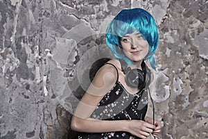 Girl in blue wig smiling with headphones on cement wall